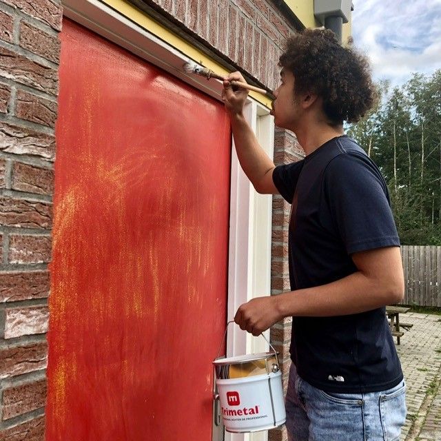 Leerling aan het schilderen met buitenkozijn van clubgebouw HSC