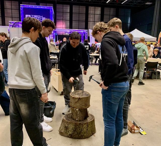 Leerlingen aan de slag met spijker slaan in een boomstam