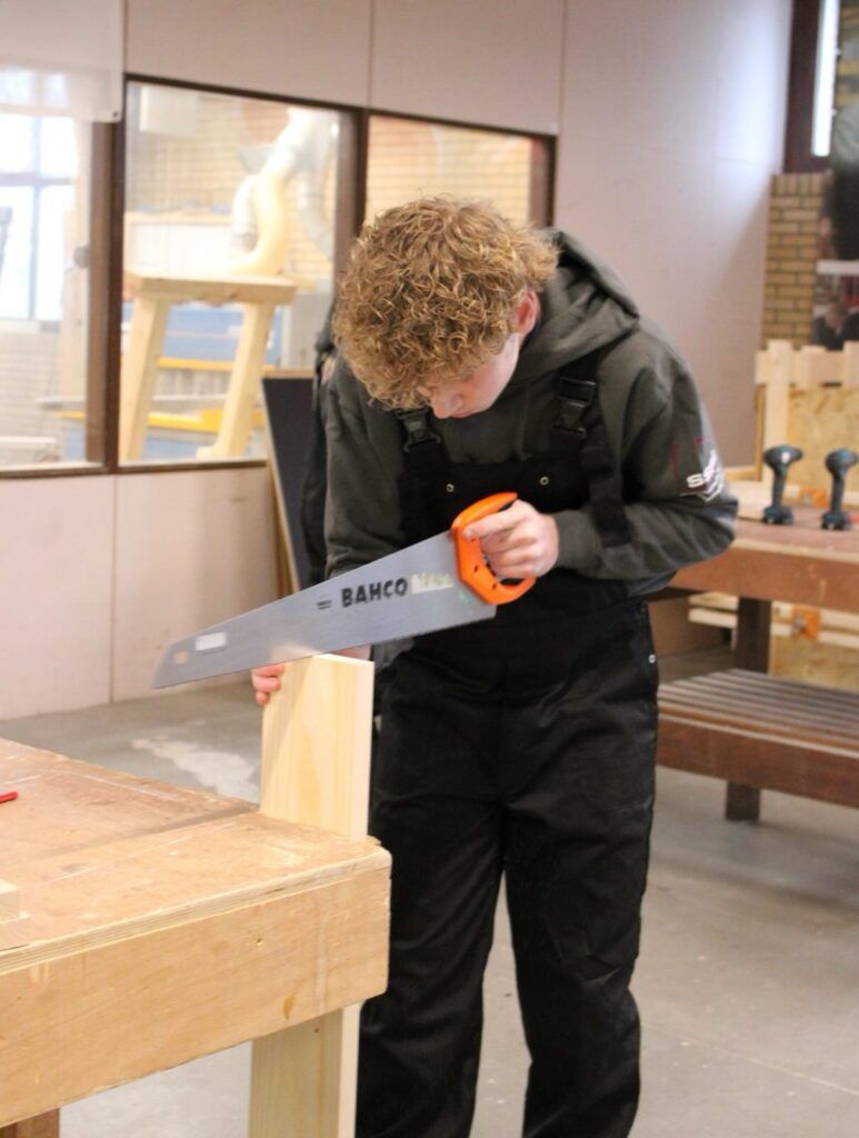 Finn werkt geconcentreerd aan zijn zaagbankje tijdens de praktijkwedstrijd